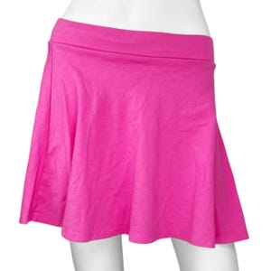 May include: A bright pink skater skirt with a wide waistband. The skirt is made of a soft, flowing fabric and flares out from the waist. The skirt is a vibrant, solid color.