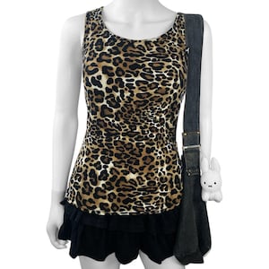 May include: A sleeveless leopard print top with a black ruffled skirt. A dark denim shoulder bag with a white plush bunny charm hangs on the side. The top features a brown and black animal print.