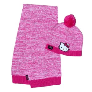 May include: A pink knit scarf and beanie set. The beanie features a Hello Kitty graphic and a pink pom-pom. The scarf and beanie are made of a pink and white speckled knit material. The beanie has a pink brim and a Hello Kitty patch.