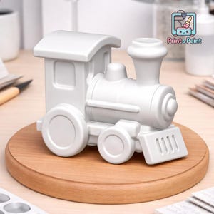 May include: A white toy train with a detailed design, including a smokestack, wheels, and a cabin. The train is displayed on a wooden base. The image includes the text "Print & Paint".