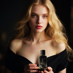 May include: A small, clear glass perfume bottle with a black cap and a gold base. The label features the text CIBIREL in a gold font, with a graphic of a mountain range at the bottom of the bottle. The bottle is held in two hands.