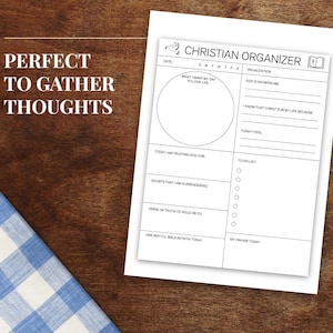 May include: A white Christian organizer sheet with a circular section and sections for daily notes. The text "PERFECT TO GATHER THOUGHTS" is on the left. The organizer is on a wooden surface with a blue and white checkered cloth.