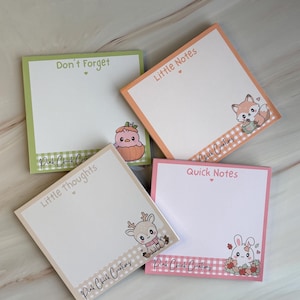 Peut inclure: Quatre blocs de notes adhésives carrés avec des bordures colorées et des illustrations de dessins animés. Les blocs portent les textes Don't Forget, Little Notes, Little thoughts et Quick Notes, ainsi que des animaux et la marque Pink Chick Creations.