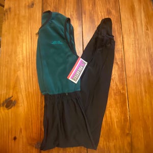 May include: A teal and black outdoor fleece and trousers set. The teal fleece vest has a black trim and the embroidered text "L.L. Bean". A "Polartec" tag is attached. The black trousers are folded next to the vest.