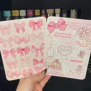 May include: Two open pink sticker sheets with bow designs and text. One sheet features multiple bow stickers, while the other has text that reads "Girls just wanna have book funds" and "She's got a book for every situation."