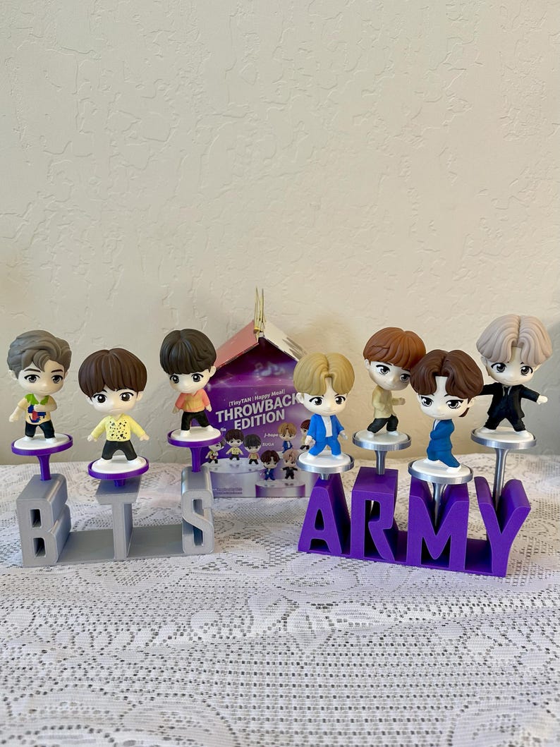 May include: A collection of small figurines of cartoon characters, each standing on a pedestal. The figurines are arranged on a table with the letters "BTS" and "ARMY" in front of them. A box with the words "THROWBACK EDITION" is visible.