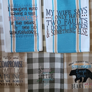 May include: A collection of kitchen towels with humorous embroidered phrases. The towels feature various colors, including blue, white, and brown, with text like "I wouldn't mind having a split personality" and "My wife says I only have two faults."