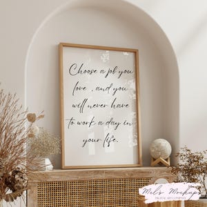 May include: A framed print with the quote, "Choose a job you love, and you will never have to work a day in your life." The frame is light brown, and the text is in black script. The print is displayed on a wooden cabinet.