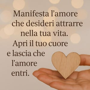 Può includere: Un cuore di legno è tenuto in una mano aperta, con il testo in italiano che recita: "Manifesta l'amore che desideri attrarre nella tua vita. Apri il tuo cuore e lascia che l'amore entri."