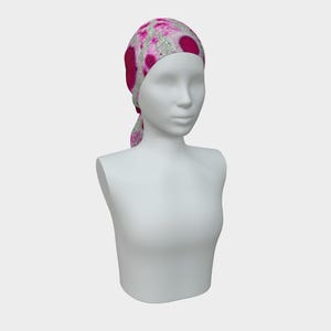 Peut inclure: Un foulard à motifs roses et blancs est présenté sur un mannequin. Le couvre-chef présente de grands motifs circulaires rose foncé sur un fond blanc et argenté. Le foulard est noué à l'arrière du cou.