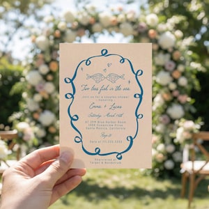 Può includere: Un biglietto d'invito beige con testo blu e un bordo decorativo. Il testo recita "Two less fish in the sea" e invita gli ospiti a un baby shower in onore di Emma e Lucas. L'evento si terrà sabato 16 marzo.