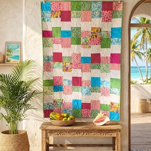 May include: A colorful patchwork quilt with squares of pink, green, blue, and floral patterns hangs on a wall. The quilt is bordered in green. A wooden bench holds a bowl of fruit and a seashell. A framed print reads "Caribbean Escape."