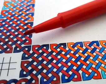 May include: A red marker pen is being used to color a detailed intricate design of a Celtic knot. The knot is colored in shades of blue, red, orange, and white.