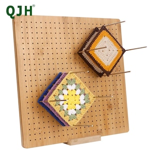 Peut inclure: Un panneau de blocage en bois avec de nombreux trous, contenant plusieurs carrés de crochet colorés. Les carrés sont dans les tons de jaune, violet, bleu, marron et crème. Le panneau porte le texte "QJH" dans le coin supérieur gauche.