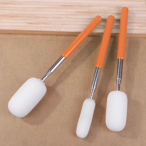 May include: Three sponge brushes with white cylindrical foam heads attached to silver telescopic metal handles. Each handle features a bright orange grip at the end, allowing for adjustable length during use for various painting or cleaning tasks.