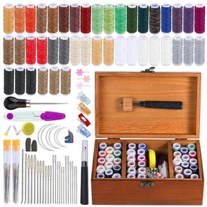 May include: A comprehensive leathercraft kit featuring a wooden box filled with spools of thread in various colors, needles, tools, and a wooden mallet. The kit includes a variety of sewing tools, including a measuring tape, awl, and thread clips.