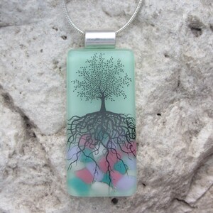 May include: A green glass pendant necklace with a black tree and roots design. The roots are surrounded by colorful glass beads.