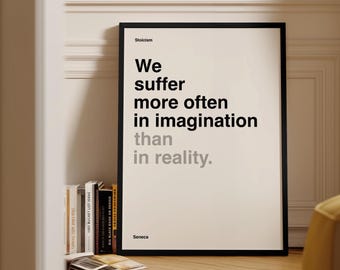 May include: A framed poster with the quote "We suffer more often in imagination than in reality" by Seneca. The text is in black and gray on a white background, with a black frame. The poster is propped against a wall.