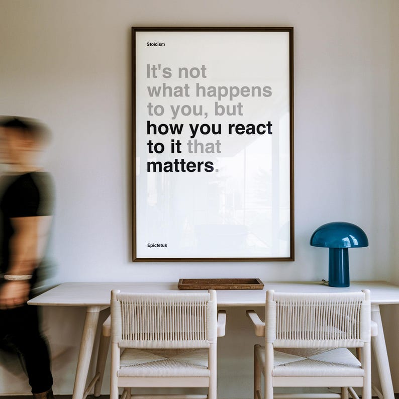 Puede incluir: Una impresi&oacute;n enmarcada con el texto "It's not what happens to you, but how you react to it that matters." se muestra sobre un escritorio blanco. Tambi&eacute;n se ven una l&aacute;mpara azul y dos sillas.