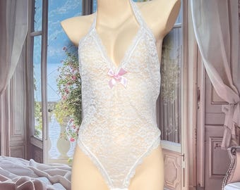 May include: A white lace bodysuit featuring a halter neckline and a small light pink ribbon bow centered at the chest. The garment is crafted from a delicate floral lace pattern with scalloped edges along the leg openings and neckline.