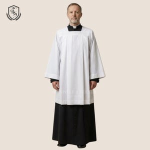 May include: A white surplice featuring a square neckline and wide sleeves, worn over a black cassock with a row of buttons down the front. The garment is plain and structured, with vertical pleats on the front of the white over-garment.