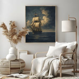 May include: A framed nautical art print depicts a tall ship sailing on a dark blue sea under a cloudy sky. The artwork is in a wooden frame and is displayed in a room with neutral decor, including a chair, throw, and floor lamp.