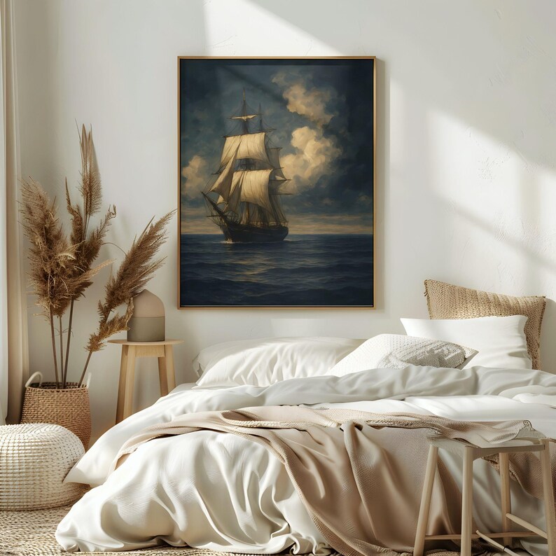 May include: A framed nautical painting depicts a tall ship sailing on a dark blue sea under a cloudy sky. The artwork features a gold frame and is displayed above a bed with white linens and a beige blanket.