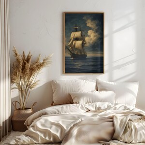 May include: A framed nautical print depicting a tall ship sailing on a dark blue sea under a cloudy sky. The artwork is displayed above a bed with cream-colored bedding and pillows. A woven basket with dried plants sits nearby.