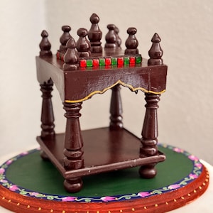 May include: A miniature, dark brown wooden table with ornate legs and a lower shelf. The tabletop is decorated with red and green accents. The table is placed on a green and red decorative base with floral patterns. A decorative piece.