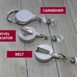 Pu&ograve; includere: Tre porta badge retrattili bianchi con diversi stili di attacco: un moschettone, una clip a coccodrillo girevole e una clip da cintura. Ogni supporto ha una cinghia di plastica trasparente con chiusura a scatto. Le parole "CARABINER", "SWIVEL ALLIGATOR" e "BELT" sono in riquadri rossi.
