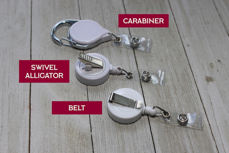 Pu&ograve; includere: Tre porta badge retrattili bianchi con diversi stili di attacco: un moschettone, una clip a coccodrillo girevole e una clip da cintura. Ogni supporto ha una cinghia di plastica trasparente con chiusura a scatto. Le parole "CARABINER", "SWIVEL ALLIGATOR" e "BELT" sono in riquadri rossi.
