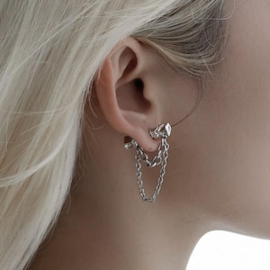 May include: Silver chain earrings with a decorative stud and dangling chains. The earrings are worn on the ear, with the chains hanging down. The earrings are a stylish accessory.