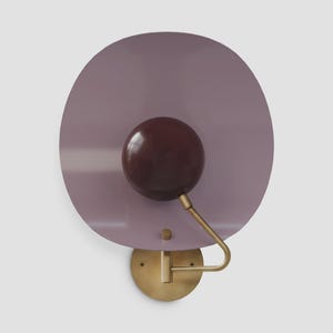 May include: A contemporary wall sconce with a circular lavender shade and a dark brown spherical light. It has a brass-coloured arm and base, offering a stylish lighting solution for any interior space.