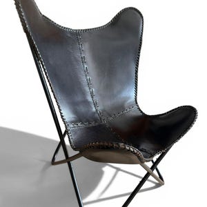 May include: A black leather butterfly chair featuring a smooth, dark surface with visible stitched seams along the edges and center panels. The seat is supported by a thin, black metal frame with a crossed base design, creating a sling-style seat.