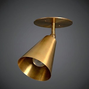 Puede incluir: Un foco de techo de latón con forma de cono. La luminaria tiene una base circular y un cabezal giratorio. El cono dirige la luz hacia abajo. La luminaria metálica tiene un color dorado cálido y está diseñada para montaje en techo.