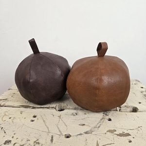 May include: Two round, stuffed objects with a textured surface and a small loop at the top. One object is dark brown, and the other is a lighter tan brown. Both items have visible seams running vertically along their rounded, bulbous shapes.