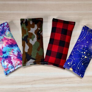 May include: Four rectangular fabric items with various patterns. One features a tie-dye design in pink, blue, and purple. Another has a camouflage pattern in green, brown, and gray. A third displays a red and black buffalo plaid. The last has a blue celestial design.