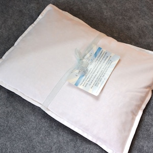 May include: A white pillow with a blue ribbon tied around it. The pillow has a white tag attached to it with the text "Cozy Nights" and information about the product.