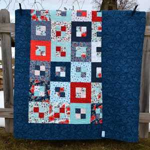 May include: A blue and white quilt with a red and white floral pattern. The quilt is hanging on a clothesline.