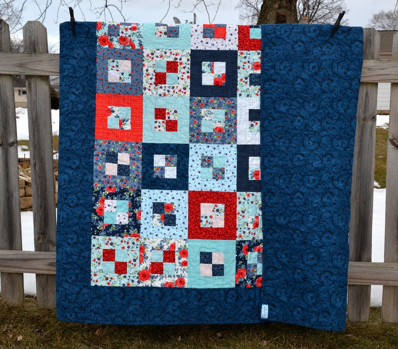 May include: A blue and white quilt with a red and white floral pattern. The quilt is hanging on a clothesline.