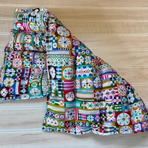 May include: A rectangular fabric heating pad featuring a vibrant, multi-colored geometric pattern. The design consists of repeating squares with intricate floral and linear motifs in shades of red, blue, yellow, green, and pink on a white background.