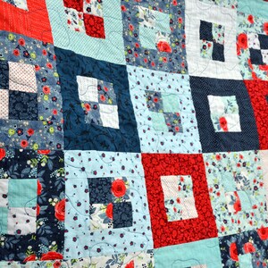 May include: A quilt made of patchwork squares in shades of blue, red, and white. The squares are arranged in a grid pattern and feature floral and geometric designs.