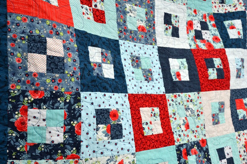 May include: A quilt made of patchwork squares in shades of blue, red, and white. The squares are arranged in a grid pattern and feature floral and geometric designs.