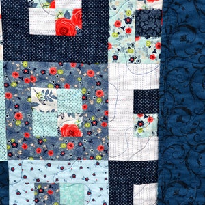 May include: A patchwork quilt with a blue and white floral pattern. The quilt is made up of squares of different fabrics, and the edges are finished with a blue fabric with a floral pattern.
