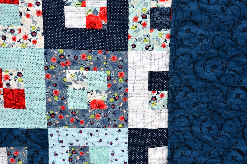 May include: A patchwork quilt with a blue and white floral pattern. The quilt is made up of squares of different fabrics, and the edges are finished with a blue fabric with a floral pattern.