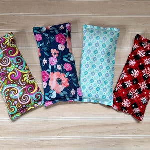 May include: Four rectangular fabric items with various patterns. One has a swirling design in brown, yellow, and purple. Another features pink flowers on a navy background. A third has a blue floral pattern, and the last has red plaid with white snowflakes.