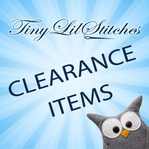 May include: A light blue background with white sunburst rays features the text Tiny Lil Stitches in a black script font above the dark blue text CLEARANCE ITEMS. A grey fabric owl plush with white felt eyes and black button pupils is visible.