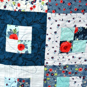 May include: A quilt made of various fabrics with floral patterns in shades of blue, white, and red. The quilt is stitched together in a patchwork design with a square pattern.