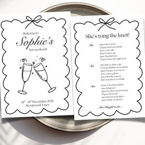 May include: Two white cards with black text and a scalloped border are displayed on a gray plate. One card reads "Welcome to Sophie's hen weekend" with champagne glasses. The other says "She's tying the knot!" with a schedule.