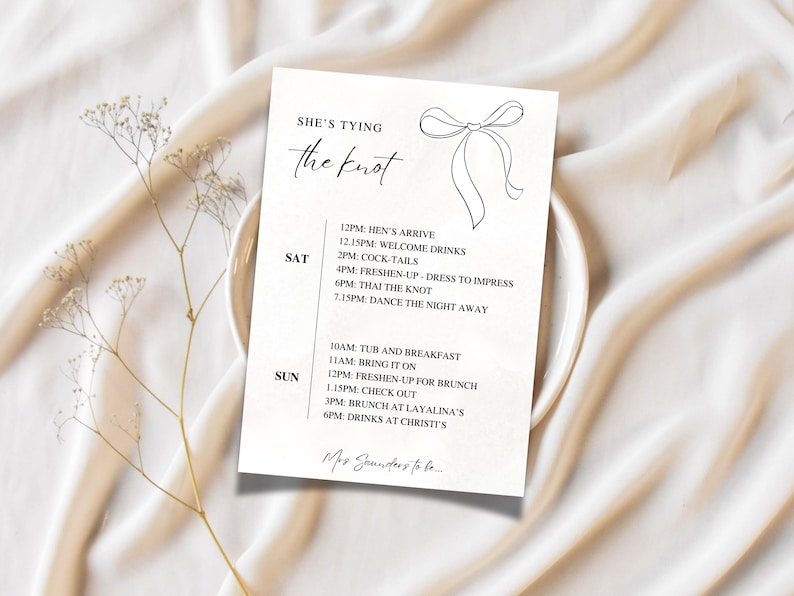 Może przedstawiać: Biała karta z napisem "She's Tying the Knot" i harmonogramem weekendu. Karta leży na białym talerzu, z suszonymi kwiatami na pierwszym planie. Harmonogram zawiera godziny i aktywności.